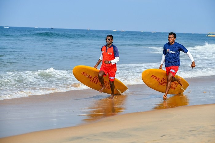 2 Drishti Lifesavers with surfboards running on the beach (1)